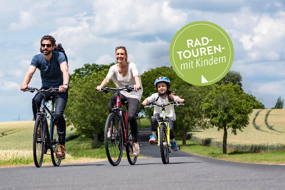 Eine dreiköpfige Familie fährt mit dem Fahrrad eine Straße im Grünen entlang