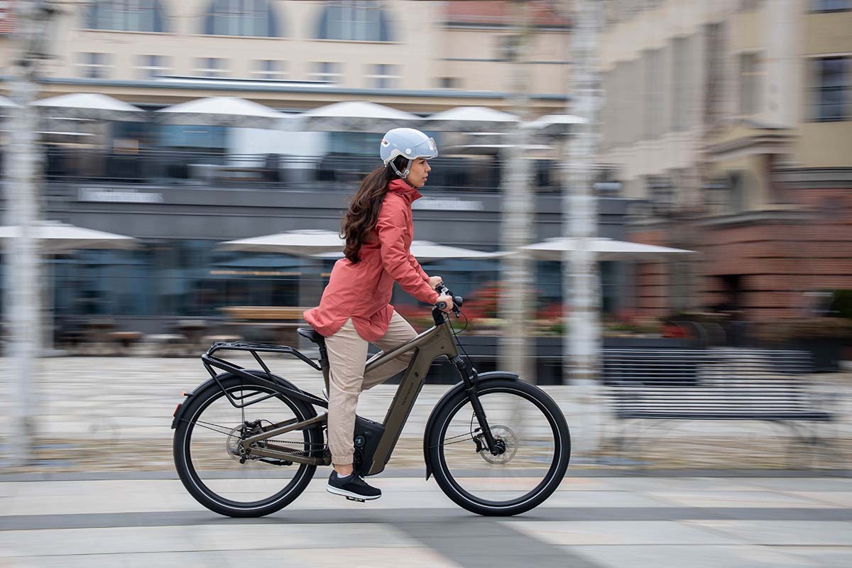 Frau fährt mit einem E-Bike durch eine städtische Gegend, der Hintergrund ist verschwommen