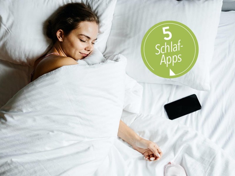Frau mit weißer Decke zugedeckt im Bett lächelt mit geschlossenen Augen, neben ihr ein Smartphone.