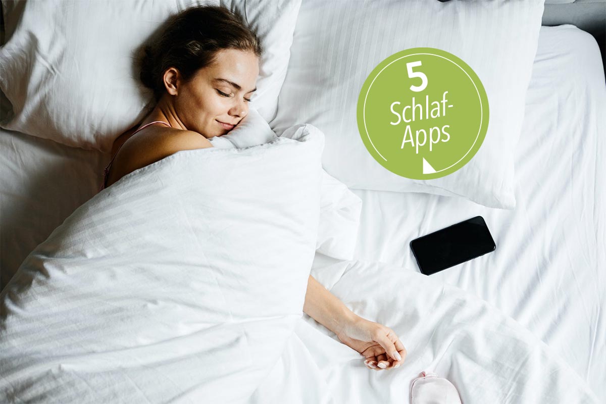 Frau mit weißer Decke zugedeckt im Bett lächelt mit geschlossenen Augen, neben ihr ein Smartphone.