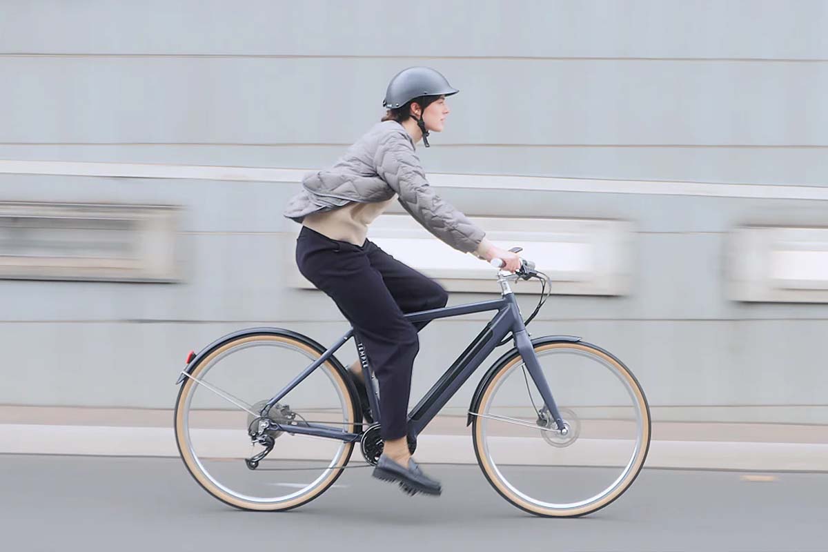 Frau fährt mit einem blauen E-Bike eine Straße entlang