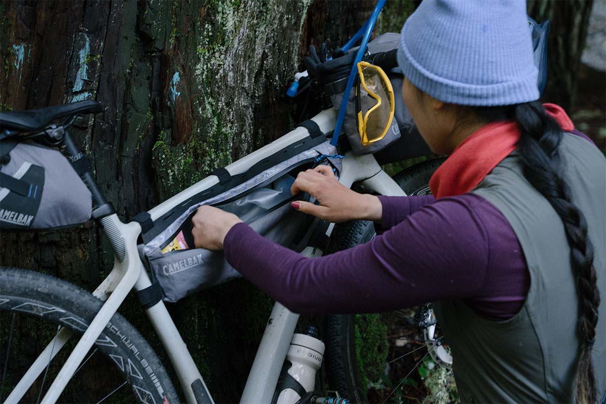 Nahaufnahme: Frau von hinten an ihrem Fahrrad, was am Baum gelehnt ist, sie sucht etwas in ihrer Rahmentasche