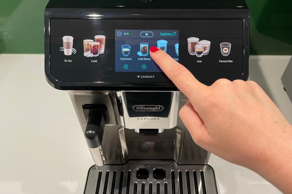 Eine Person wählt am Touch-Display des De'Longhi-Kaffeevollautomaten ein Getränk aus.