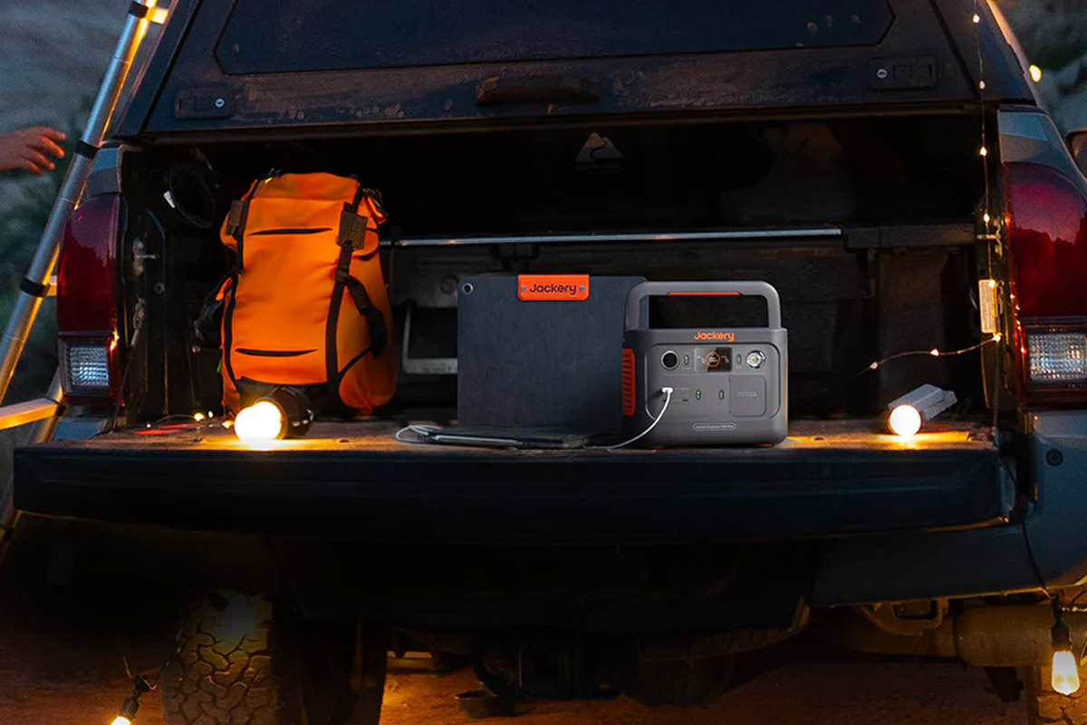 Die Explorer 300 Plus in einem geöffneten Kofferraum neben dem passenden Solarpanel, einem Rucksack und mit einer Lichterkette beleuchtet.