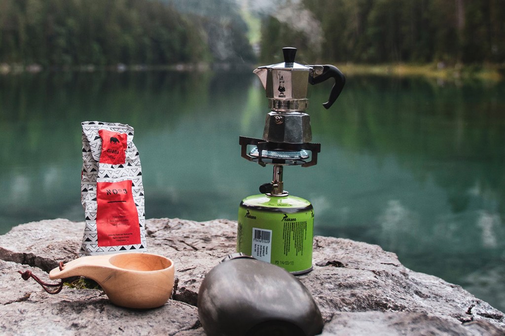 Esspressokocher steht auf einem Gaskocher vor einem See.