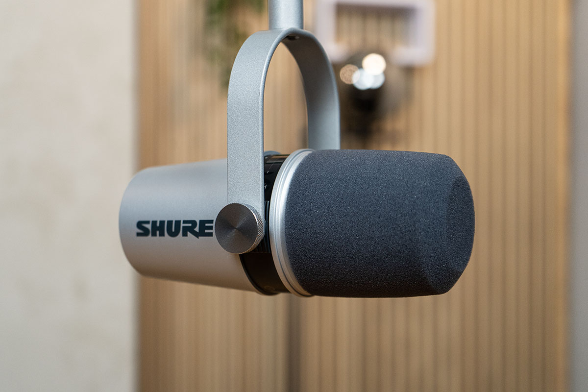 Das silberne Mikrofon Shure MV7 hängend vor einer Holzwand