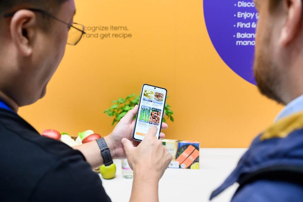 Zwei Menschen schauen auf ein Smartphone auf dem die Samsung Food App geöffnet ist.