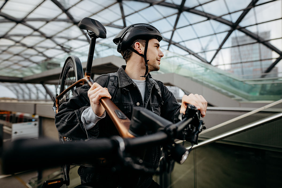 Man trägt E-Bike in Bahnhofshalle auf den Schultern.