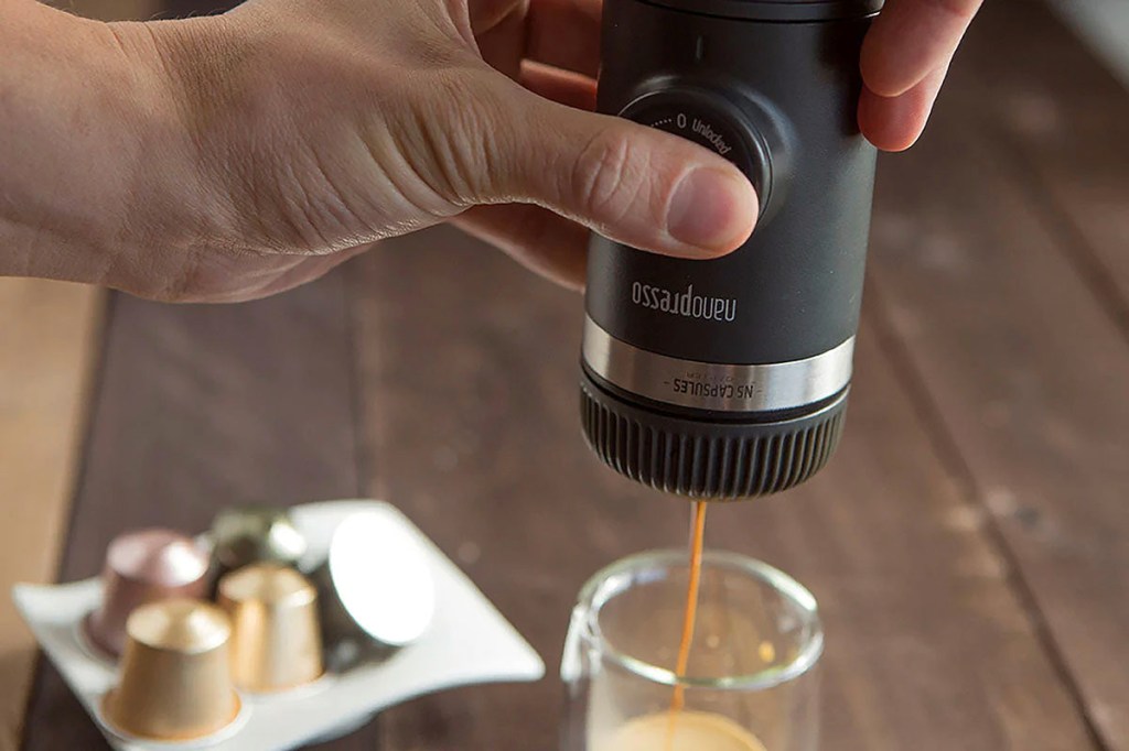 Hand die eine Handpresse von Wacaco hält und so Espresso durch Druck auf die Handpresse kocht, der dann in ein Glas tröpfelt.