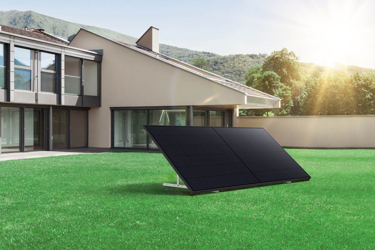 Ein Solarpanel steht in einem grünen Garten vor einem Einfamilienhaus in der Sonne.