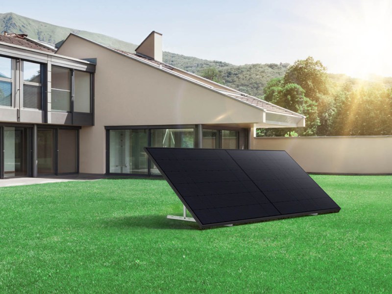 Ein Solarpanel steht in einem grünen Garten vor einem Einfamilienhaus in der Sonne.