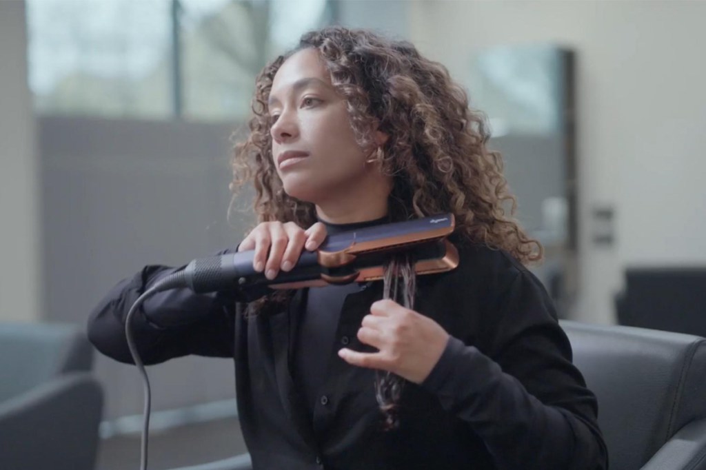 Eine Frau mit Locken zieht eine Haarsträhne mit dem Dyson Airstrait glatt.