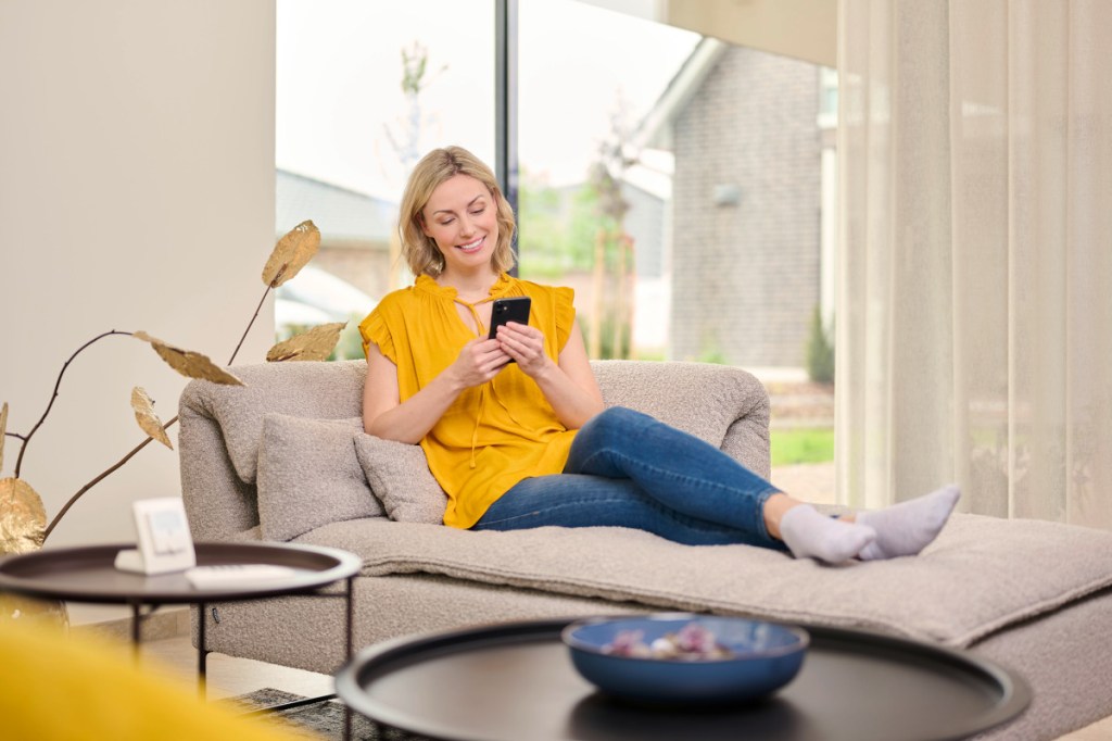 Eine Frau sitzt mit ihrem Smartphone auf der Couch.