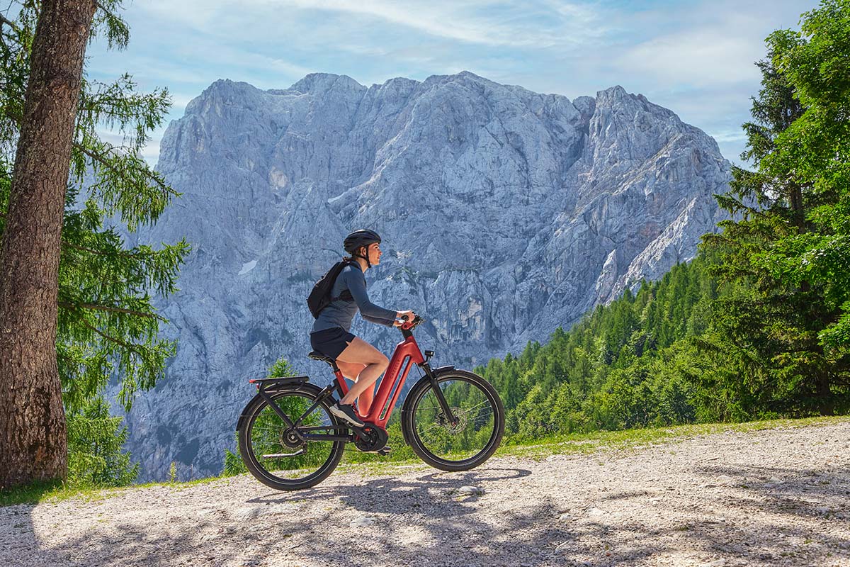 Frau fährt mit einem roten E-Bike auf einer Straße, im Hintergrund Bergkulisse im Sonnenschein