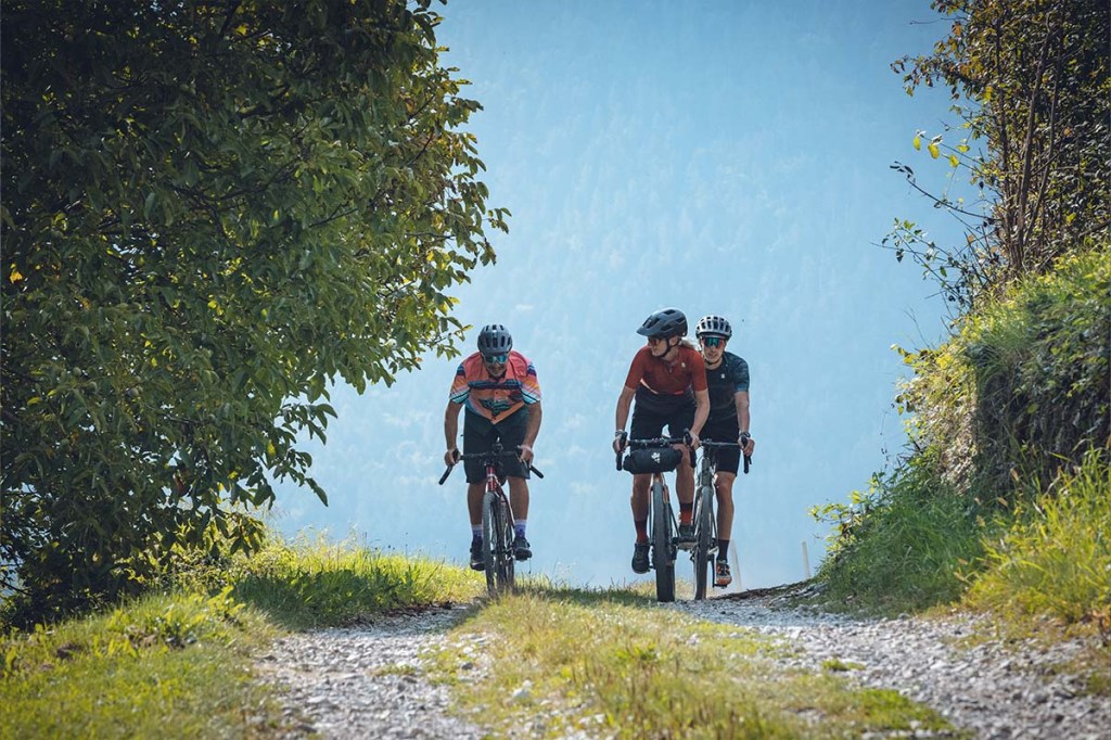 Drei Radfahrer fahren nebeneinander eine Schotterpiste lang
