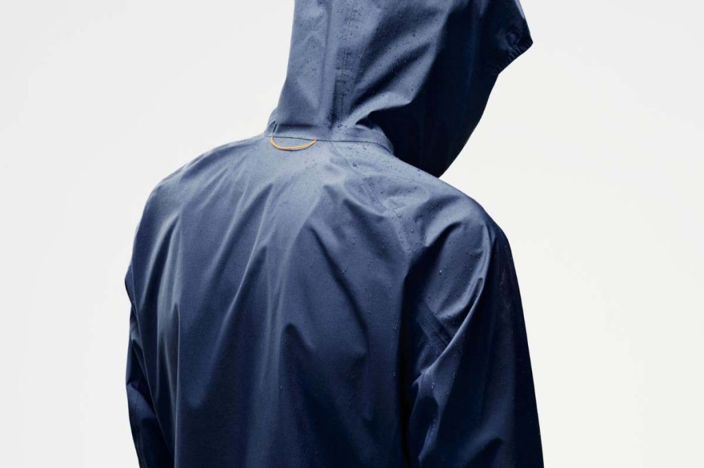 Person von hinten, trägt eine blaue Regenjacke und hat die Kapuze auf