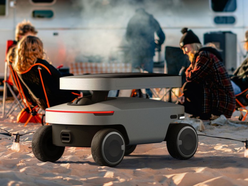 Der neue Solar Mars Bot auf einem Sandstrand. Im Hintergrund eine Camping-Szene mit Lagerfeuer.