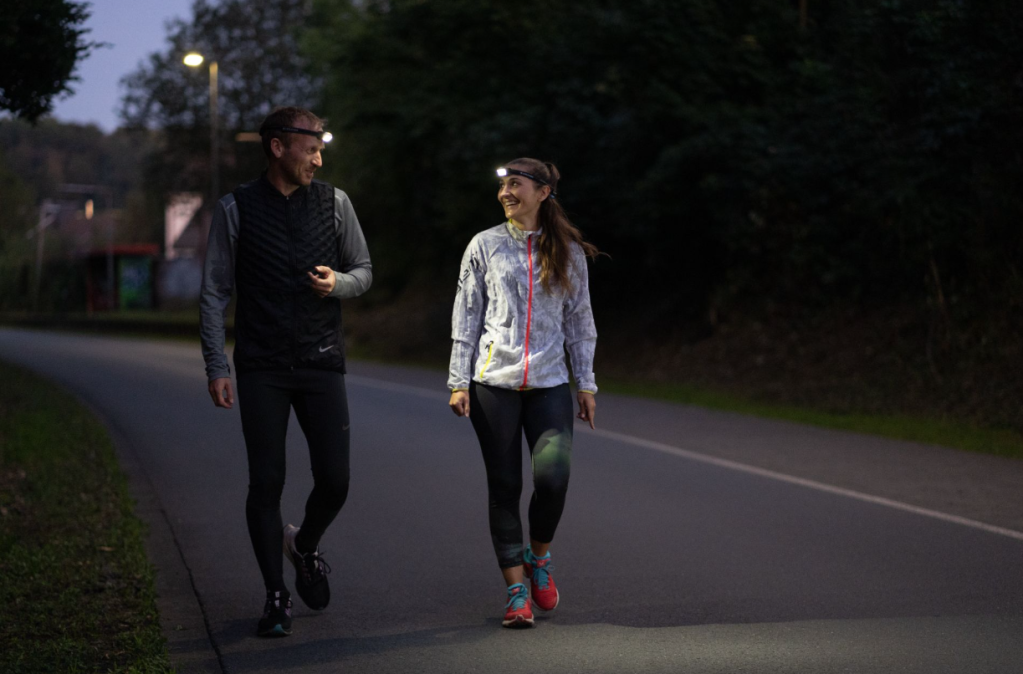Mann und Frau beim Joggen während der Dunkelheit. Beide tragen eine Stirnlampe um während der Winterzeit gut zu sehen und gut gesehen zu werden.