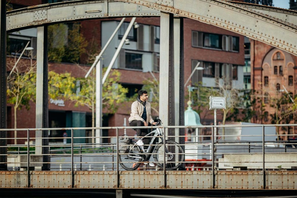 Mann mit E-Bike, fährt in einem städtischen Gebiet über eine Brücke