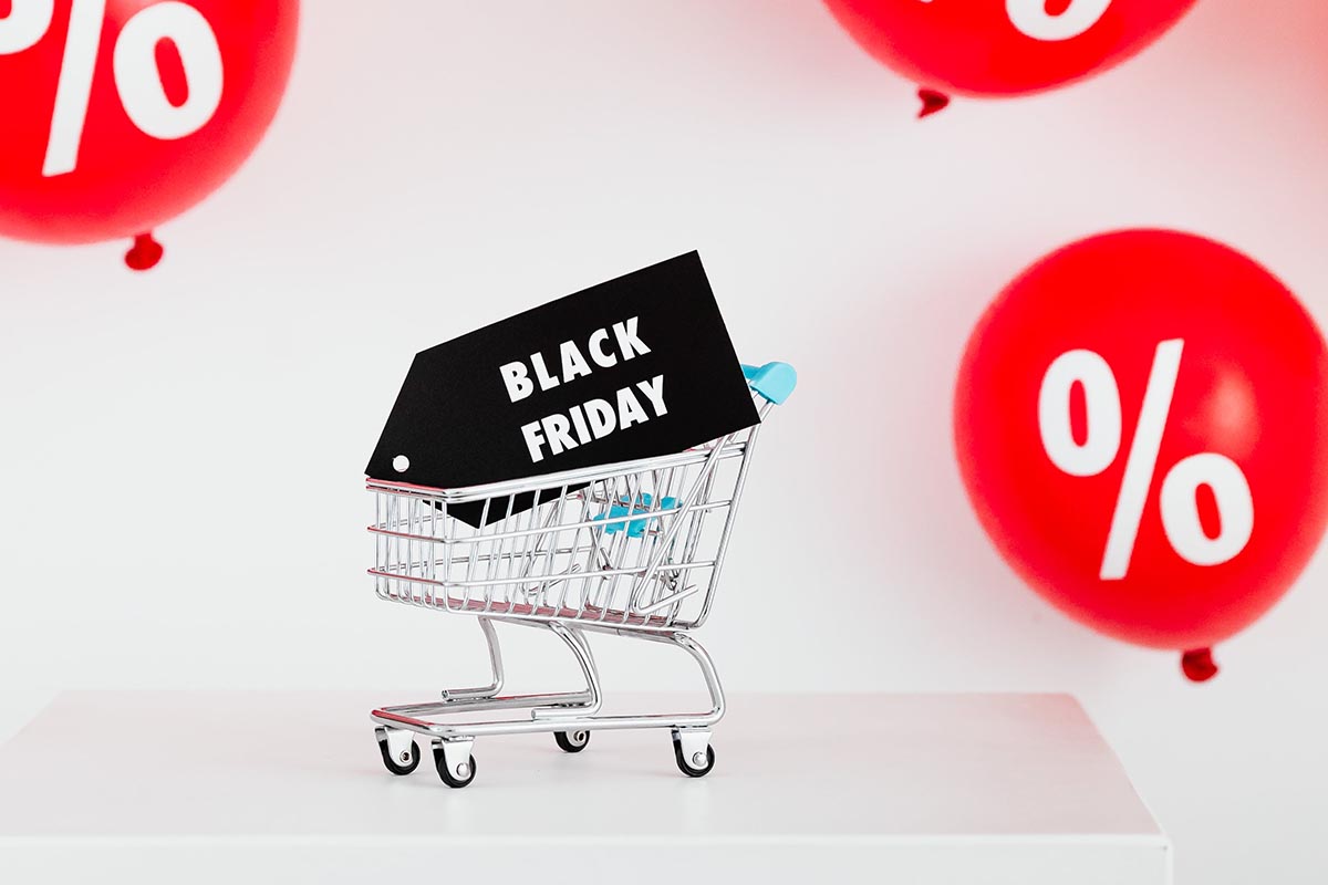 Einkaufwagen mit einem Black Friday Schild, im Hintergrund Ballons mit Prozentzeichen