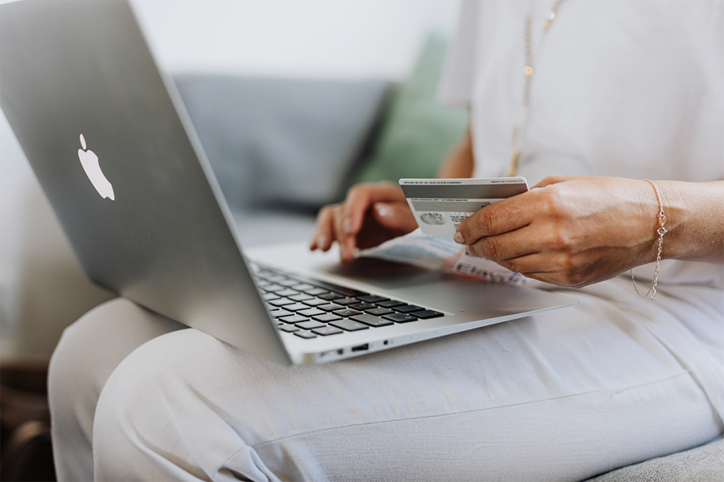 Sitzende Person mit einem Computer auf dem Schoß und einer Kreditkarte in der Hand