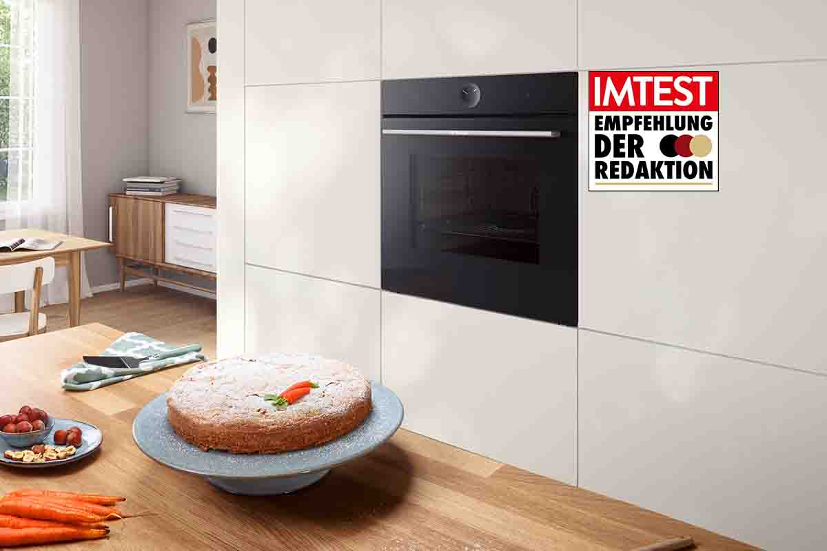 Der Bosch-Einbaubackofen in einer weißen Küchenzeile. Auf der Arbeitsfläche davor stehen ein gebackener Möhrenkuchen sowie Backutensilien. Das IMTEST-Siegel "Empfehlung der Redaktion" ist zu sehen.