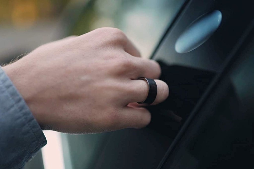 Von links reinragende Hand mit schwarzem Ring an schwarzer spiegelnder Oberfläche