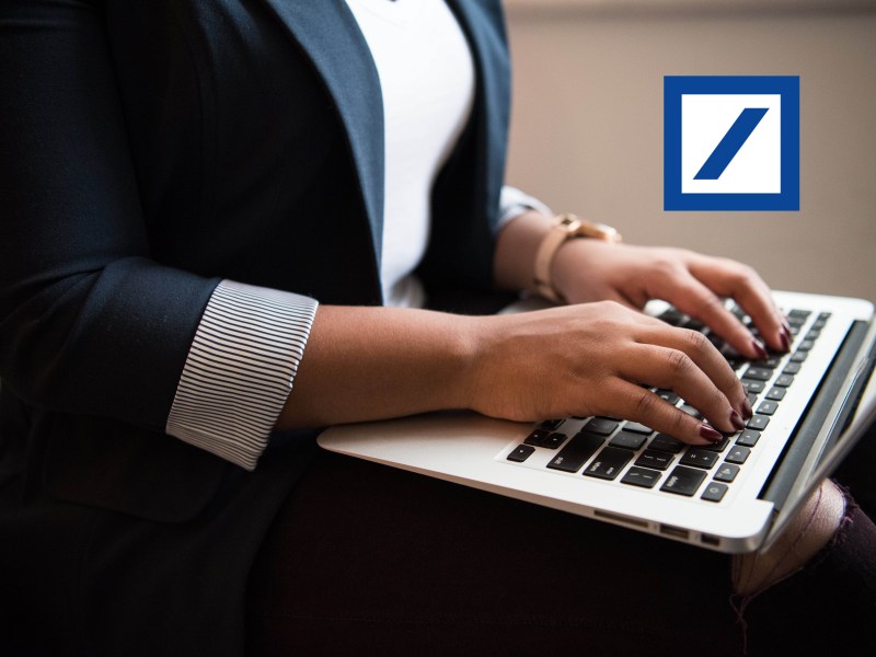Eine Person tippt auf einem Laptop, daneben ist ein Logo der Deutschen Bank zu sehen.