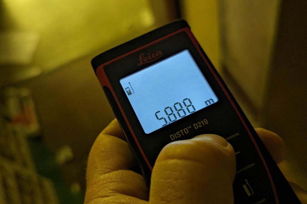 Eine Hand hält eines der Messgeräte, ein Laser-Entfernungsmesser. Auf dem Display steht 5,888 m