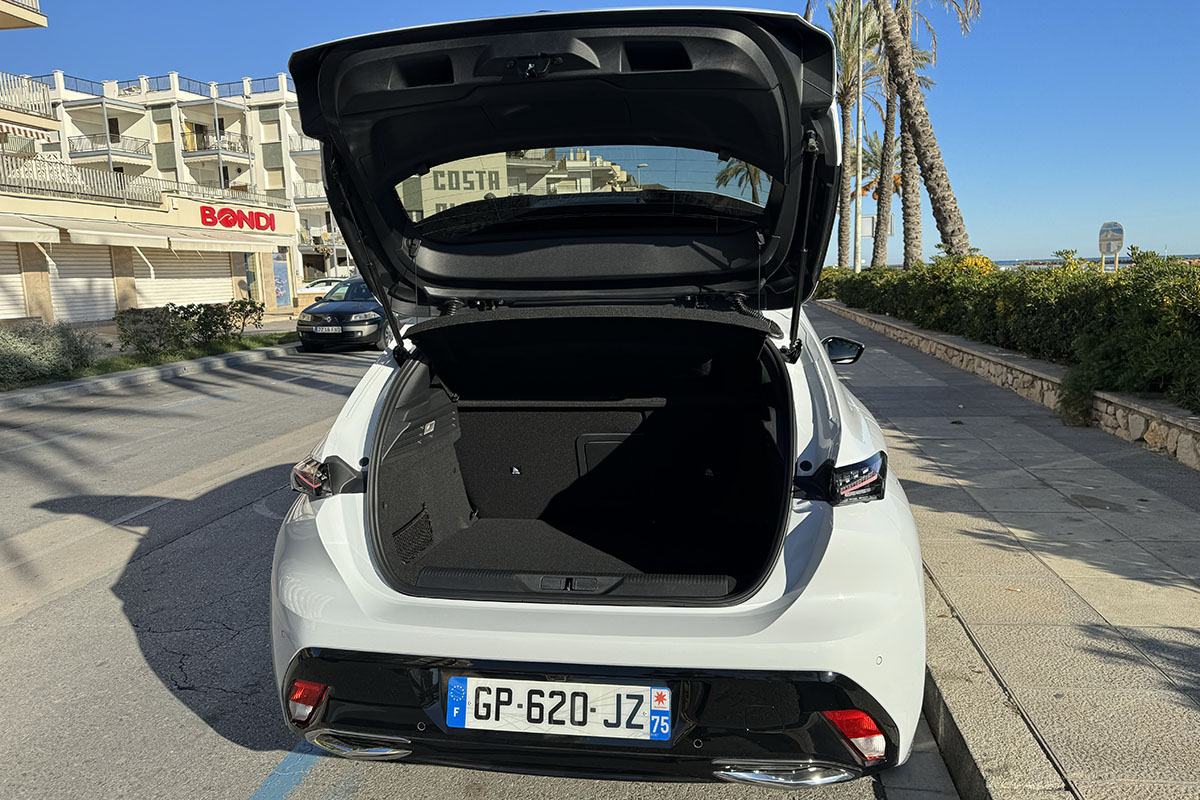 E-Auto Peugeot E-308 parkend am Straßenrand vor Stadtkulisse mit geöffneter Kofferraumklappe.