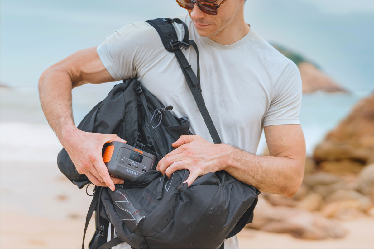 Eine Person steckt in einem Strand-Setting die Jackery Explorer 100 Plus in einen Rucksack.