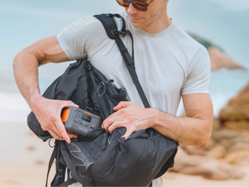 Eine Person steckt in einem Strand-Setting die Jackery Explorer 100 Plus in einen Rucksack.