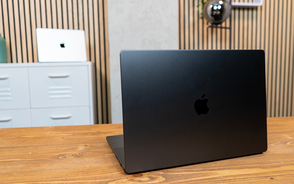 Ein dunkles Macbook Pro aufgeklappt mit dem Rücken zur Kamera fotografiert. Im Hintergrund ein silbernes Notebook.