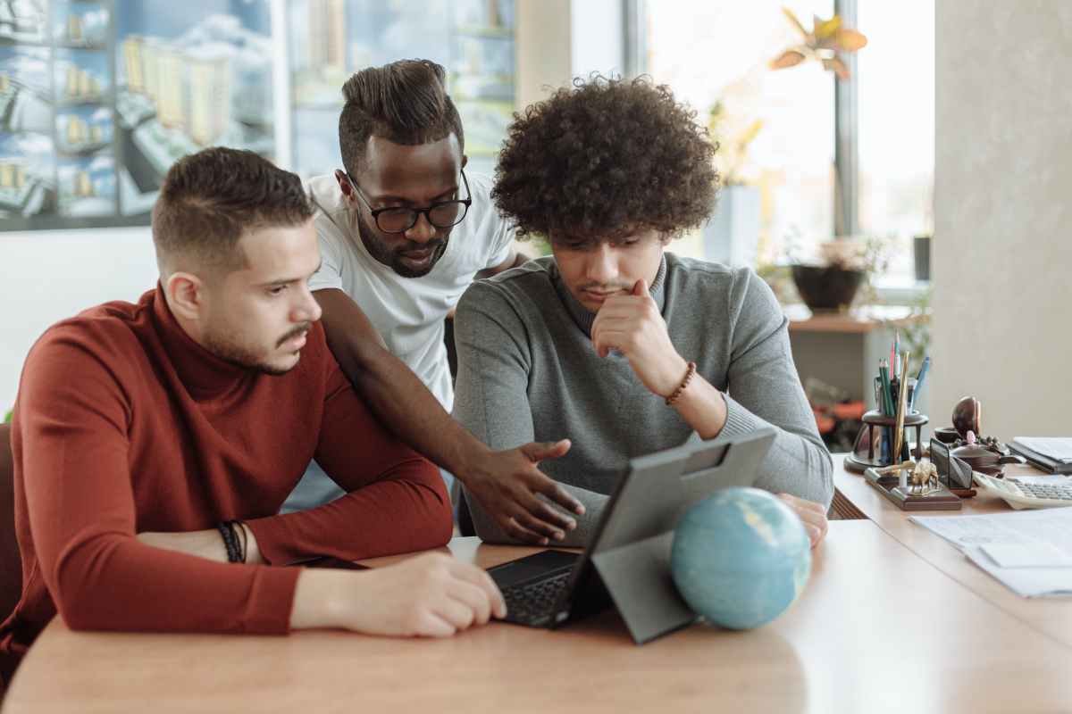 Drei junge Männer in einem Büro auf ein Tablet schauend