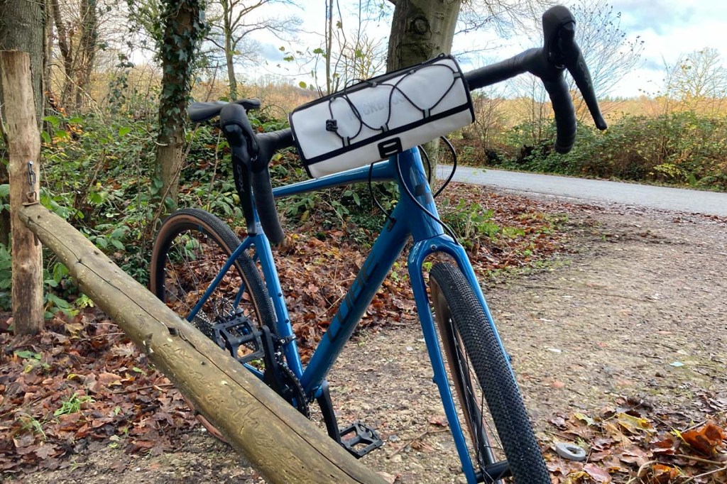 blaues Fahrrad im Wald an einen Balken gelehnt, es hat eine weiße Lenkertasche