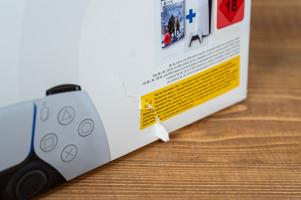 Fotografie einer leicht eingerissenen PS5-Packung auf einem Holztisch.