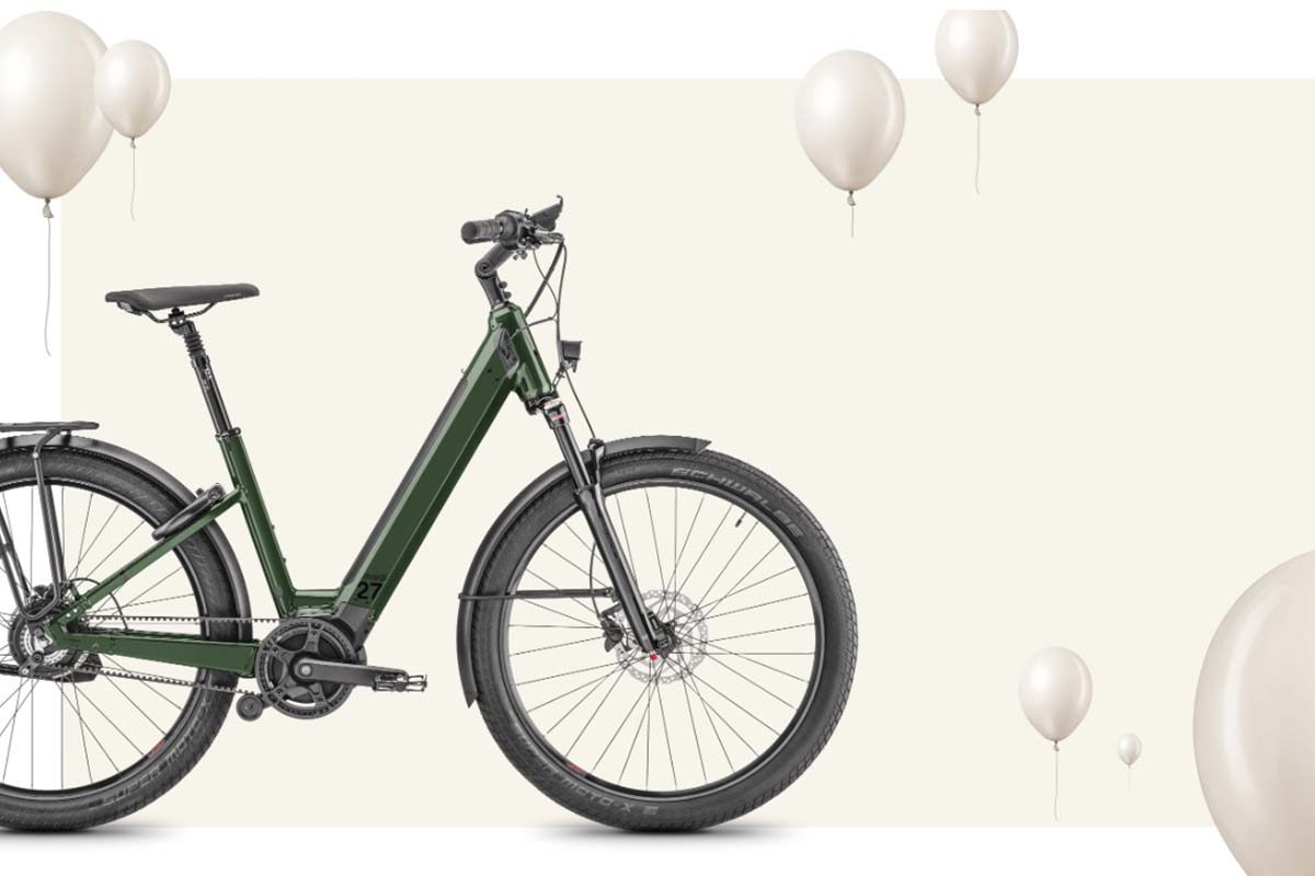 Anschnitt eines grünen E-Bikes, welches von links ins Bild gefahren kommt auf einem beigen Untergrund, dazu Luftballons