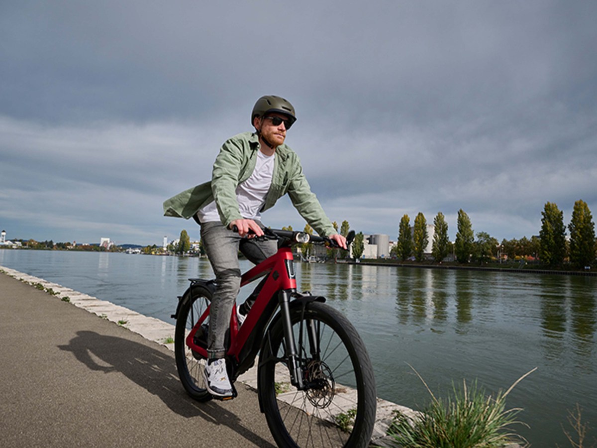 Mann fährt mit einem roten E-Bike einen Weg an einem Fluss entlang