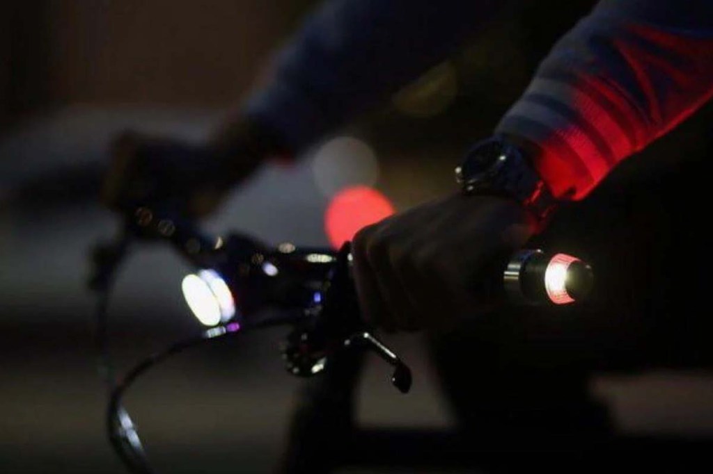 Blinklicht für Lenkerrohr an einem Lenker, es ist dunkel, man sieht den Fahrradlenker mit Armen am Lenker im Anschnitt