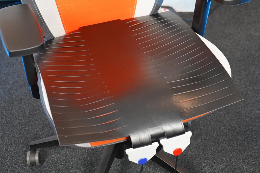 Ein orangefarbener Gaming-Stuhl mit einer Druckmatte, vorne sind die Anschlüsse mit Kabeln