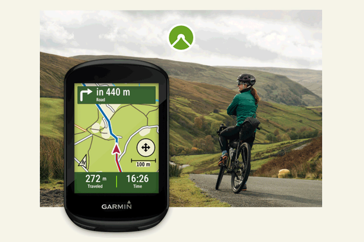 Garmin-Navigationsgerät mit Karte im Display, vor dem HIntergrund einer Radfahrerin in einer Berglandschaft.
