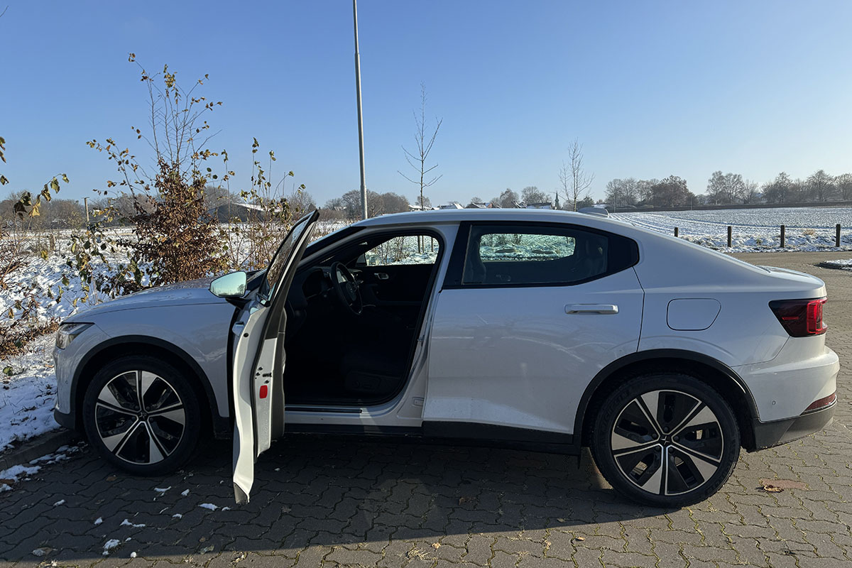 E-Auto Polestar 2 (MY24) Seitenaufnahme auf einem leicht eingeschneiten Parkplatz mit geöffneter Fahrertür.