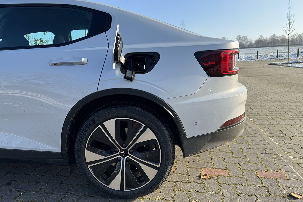 E-Auto Polestar 2 (MY24) Seitenaufnahme auf einem leicht eingeschneiten Parkplatz mit Detailansicht des geöffneten Tank-Ladedeckels.