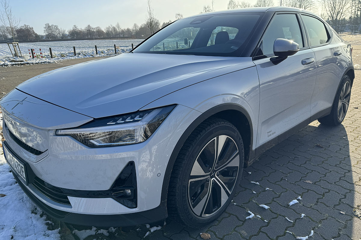 E-Auto Polestar 2 (MY24) schräge Frontalaufnahme auf einem leicht eingeschneiten Parkplatz mit Ansicht des Wagens.