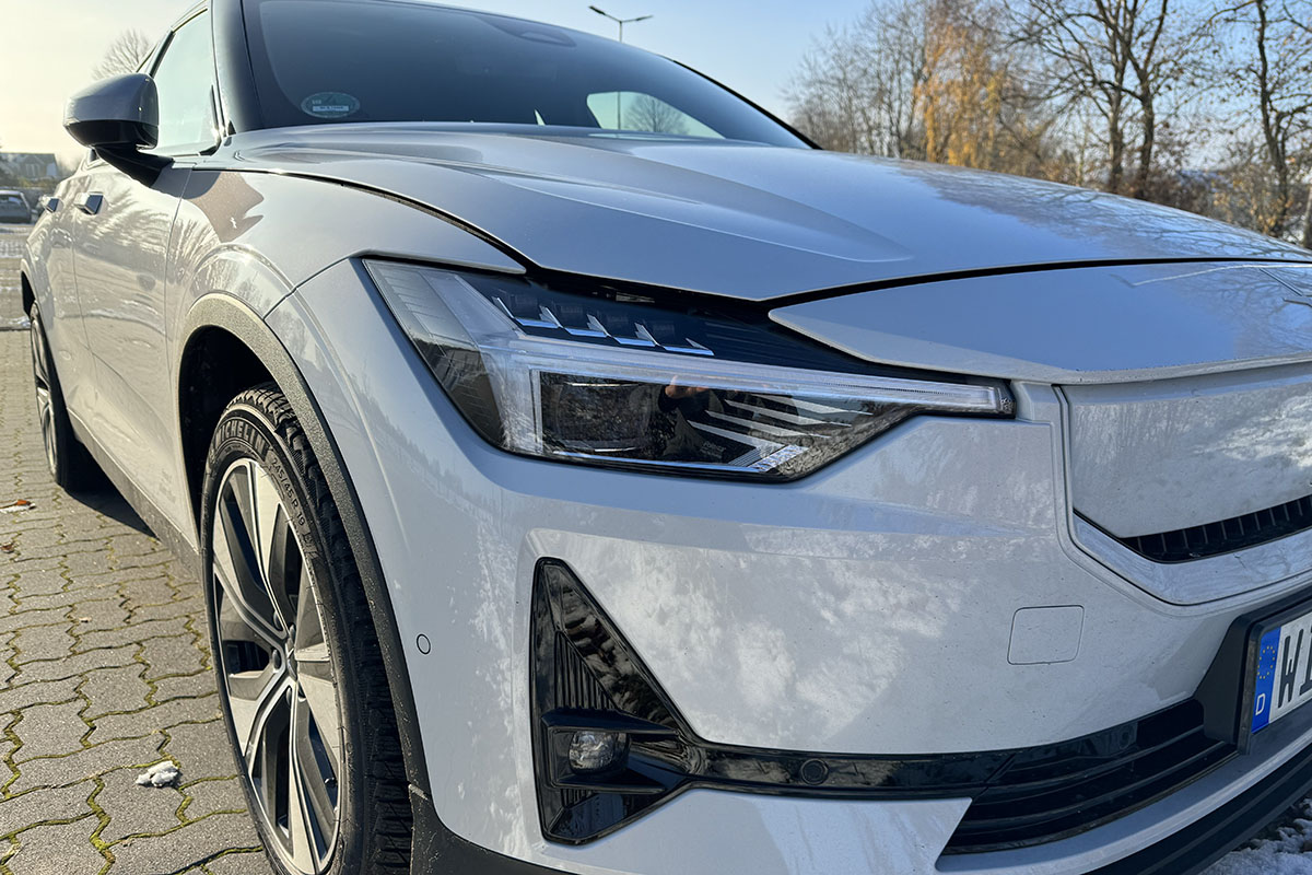 E-Auto Polestar 2 (MY24) schräge Frontalaufnahme auf einem leicht eingeschneiten Parkplatz mit Ansicht des rechten Vorderlichts.