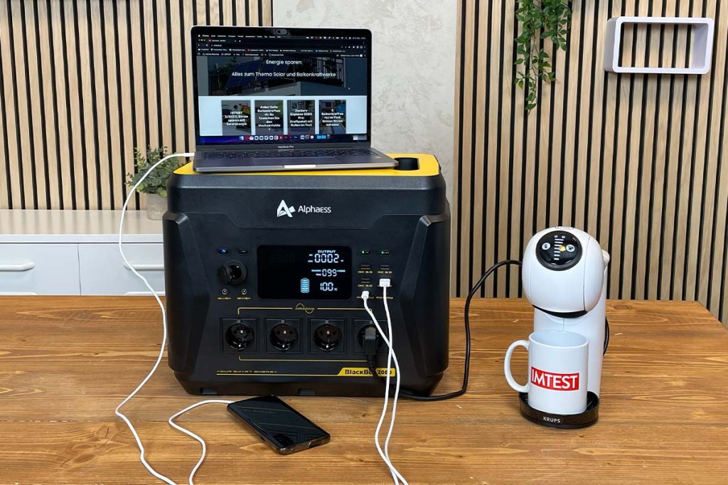 Ein Laptop, ein Smartphone und eine Kapsel-Kaffeemaschine sind an der AlphaESS BlackBee 2000 angeschlossen.
