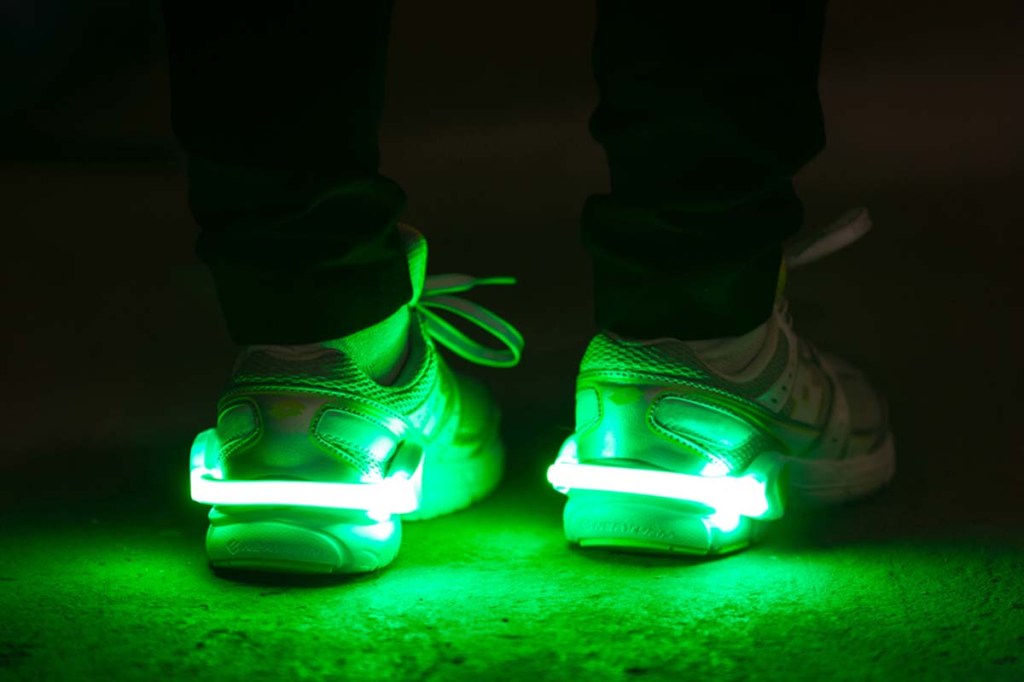 Nahaufnahme Schuhe von hinten in der Dunkelheit, die Schuhe sind mit einem LED-Clip ausgestattet, der um die Verse haftet