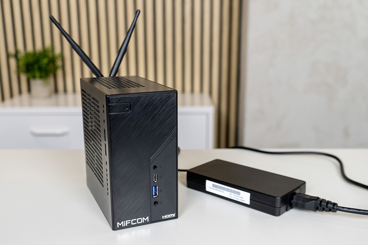 Der Mini-PC MIFCOM DekMini steht mit seinem Netzteil auf einem Tisch.