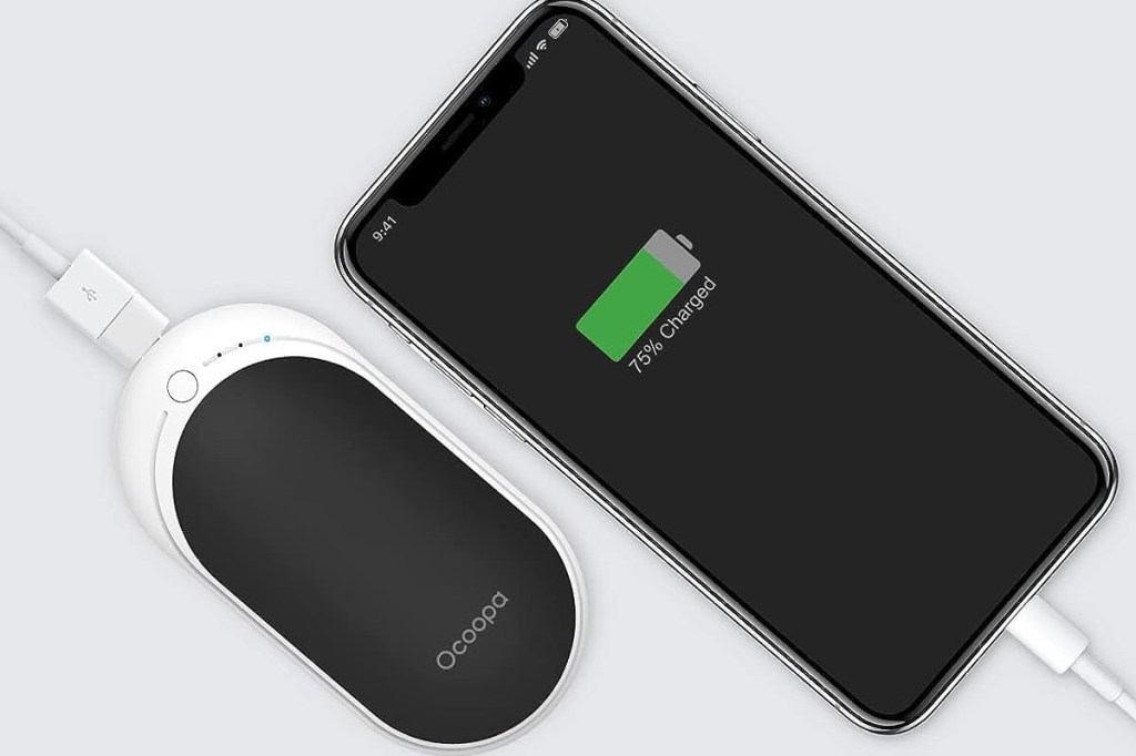 Schwarzes Smartphone liegt auf heller Fläche schräg rechts mit grüner Batterie Anzeige an weißem Kabel angeschlossen, daneben schräg links ein weiß schwarzes Gerät, das aussieht wie eine Maus, ebenfalls an einem Kabel angeschlossen