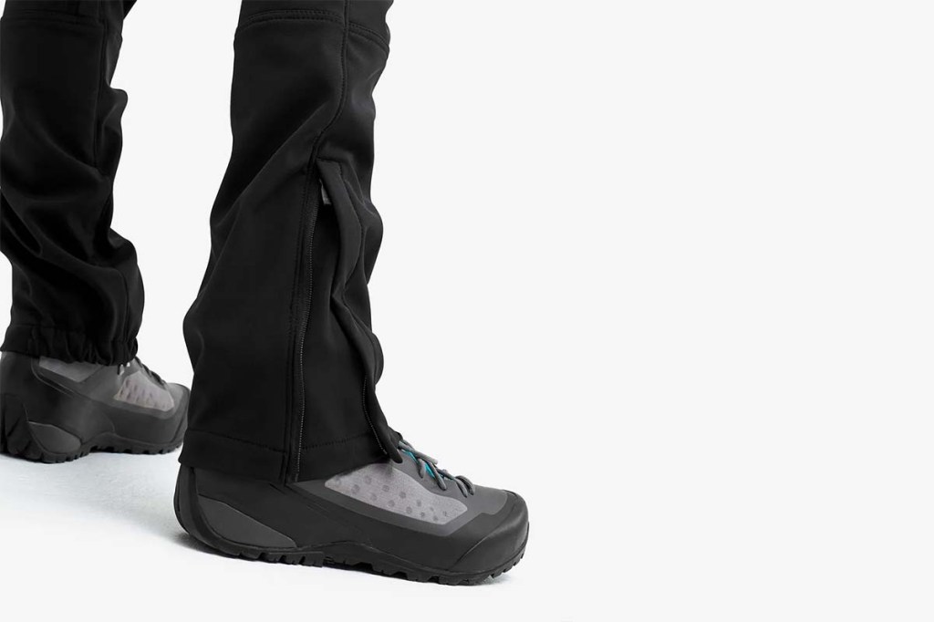 Bein, welches man nur von Fuß bis Knie sieht, bekleidet mit einer schwarzen Hose und Trekking-Schuhen. DIe Hose hat einen Reißverschluss, dass sie gut über die Schuhe passt